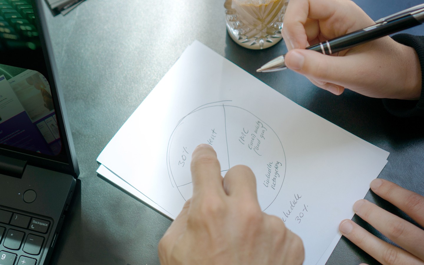 Two pairs of hands pointing to diagram on piece of paper, with coffee in background