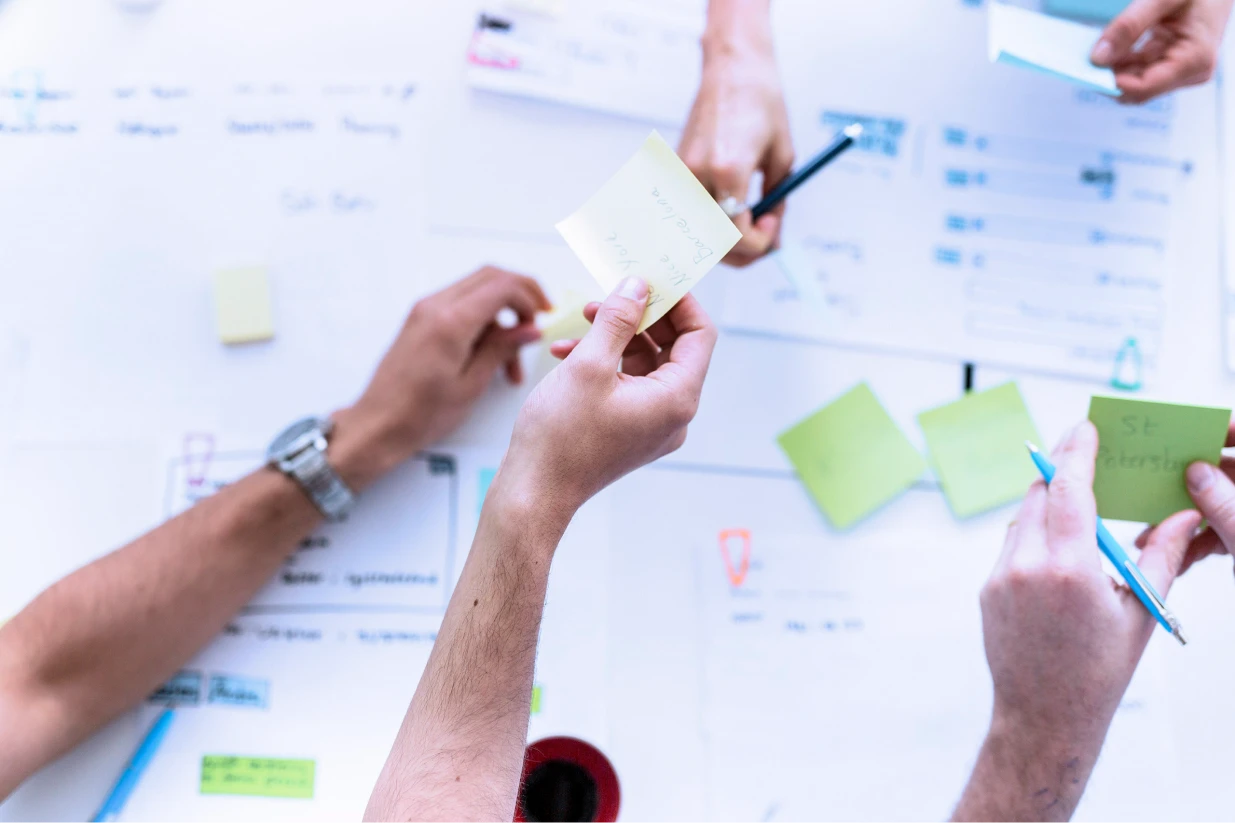 Top down view of colleagues reviewing sticky notes on a large table. 