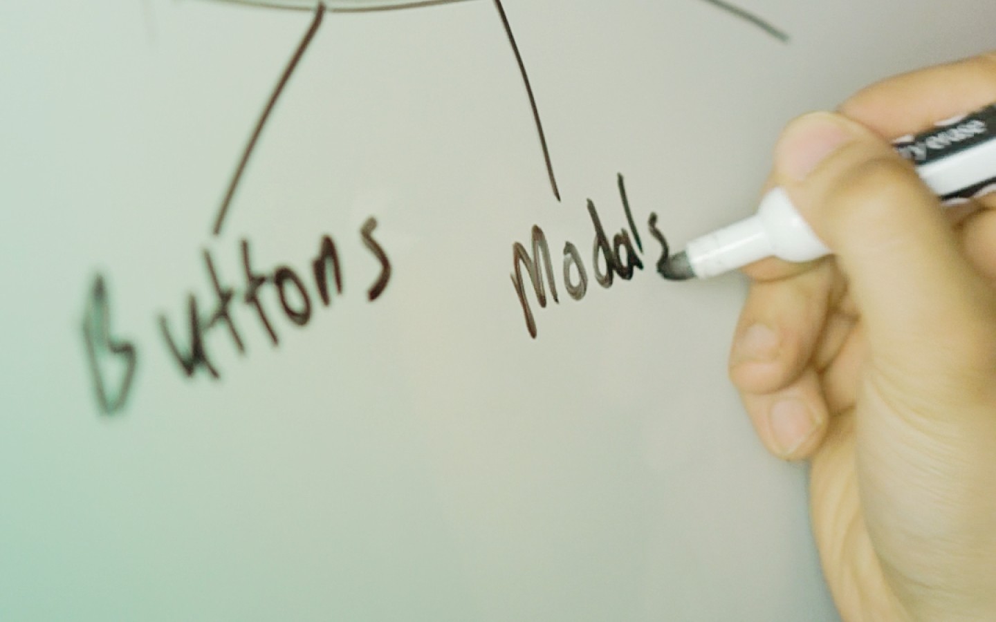 Hand writing on whiteboard with marker words 'buttons' and 'modals'