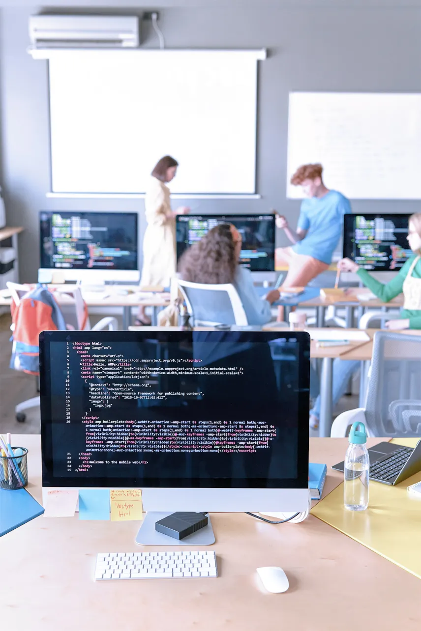 Colleagues working collaborating on work stations, with computer screens showing lines of code in the background. 