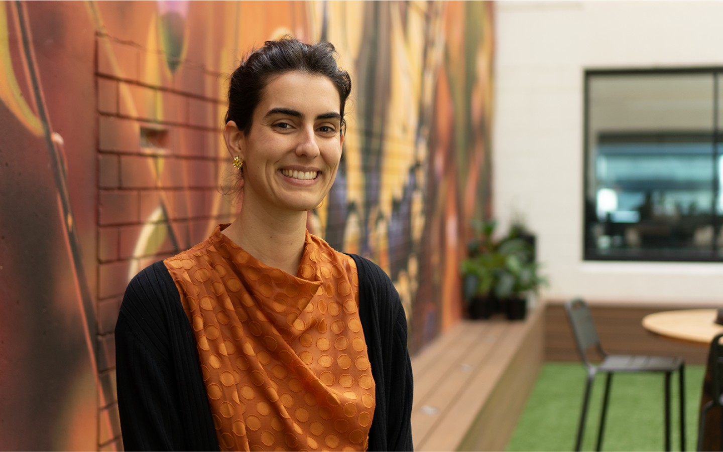 Image of woman smiling outdoors, standing against illustrated wall mural