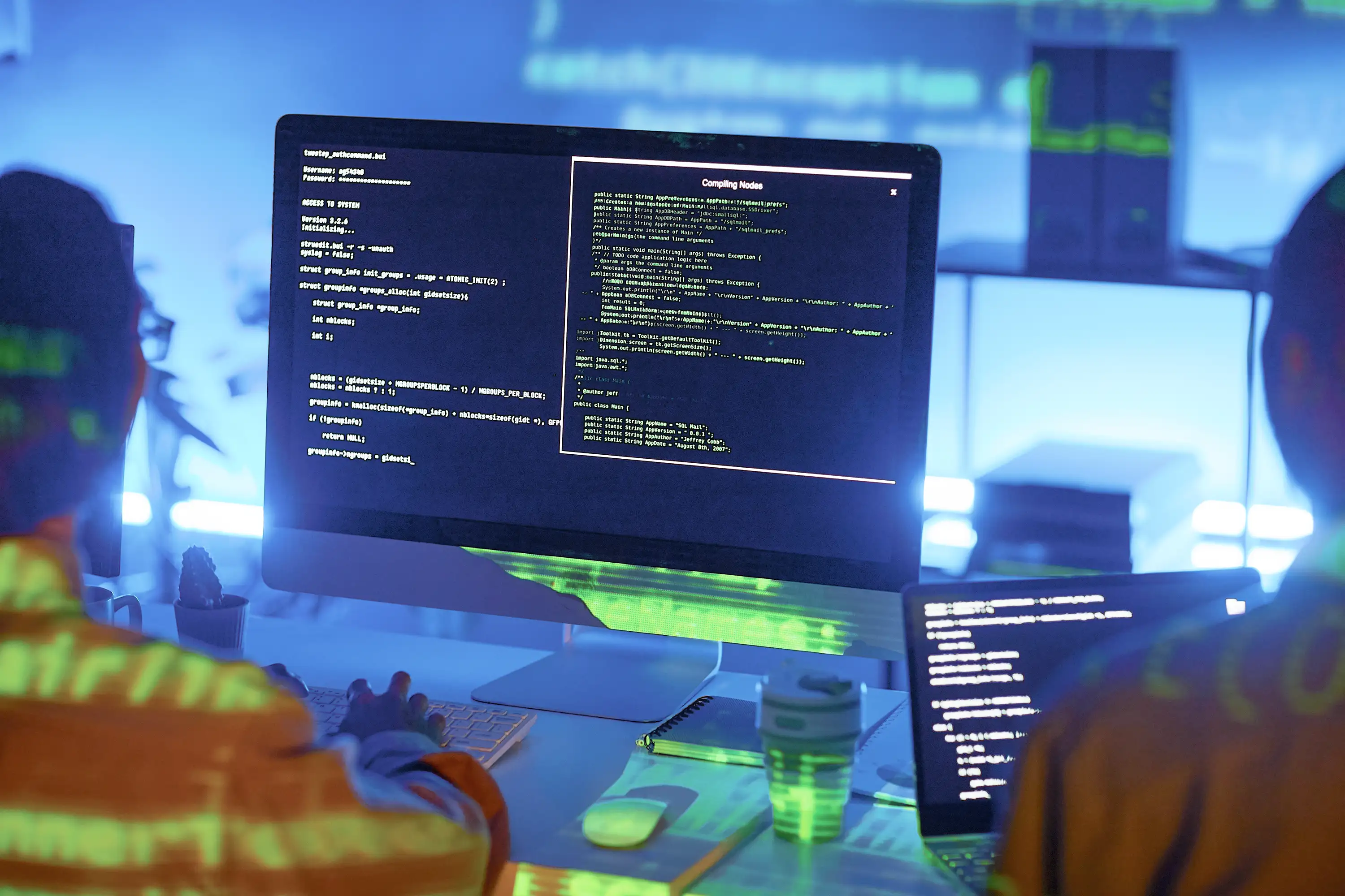 Colleagues reviewing lines of code on desktop and laptop
