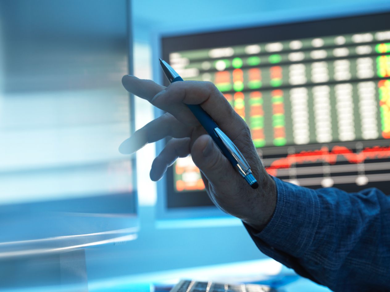 close of up hand holding pen against computer screens. 