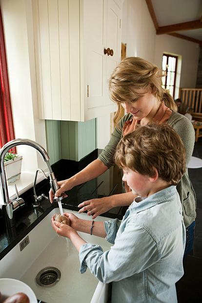 Mother and son washing vegetables under filtered water at the kitchen tap