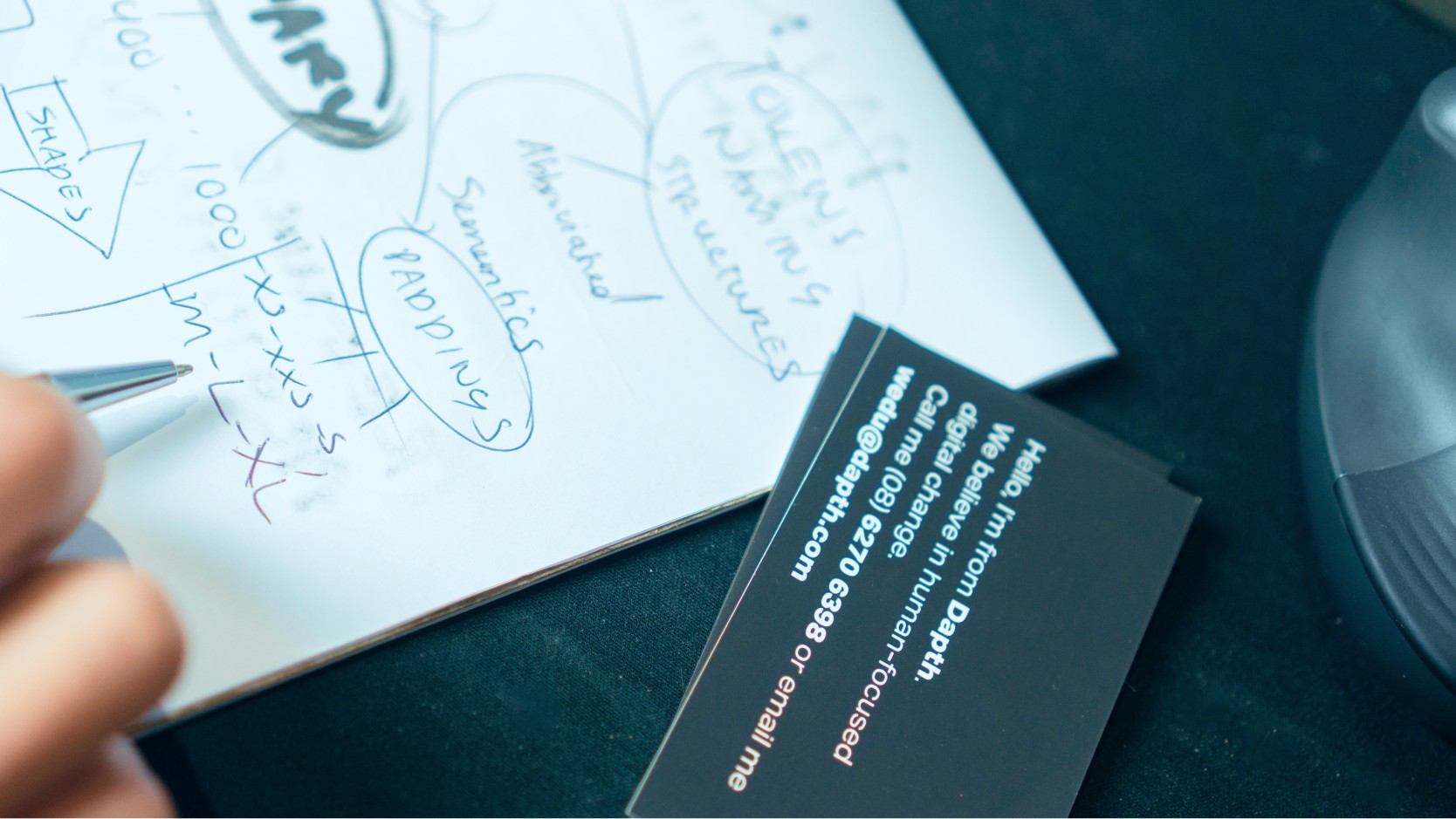 Image of hand writing / brainstorming on a notepad.  With business cards visible on the side.