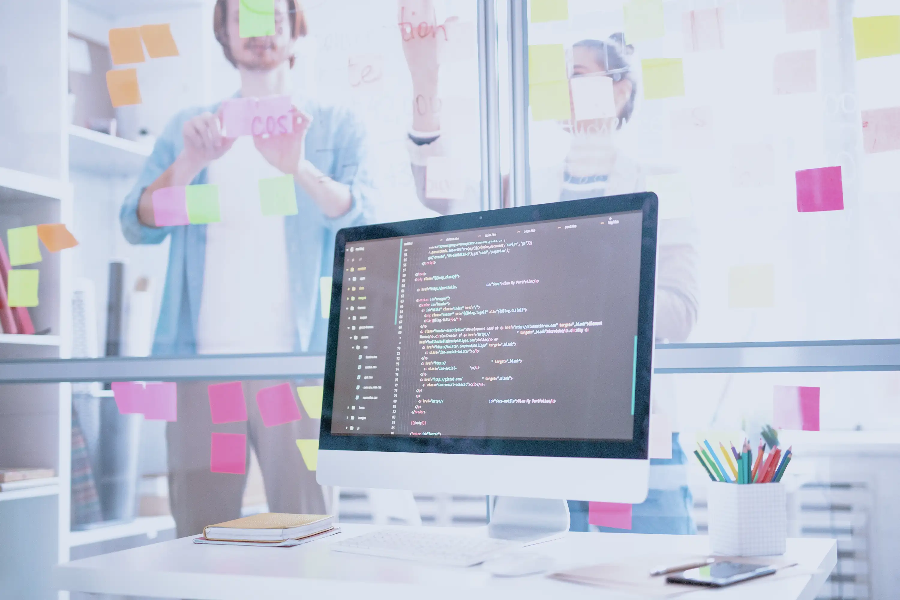 Computer screen showing lines of code with co-workers working in the background. 