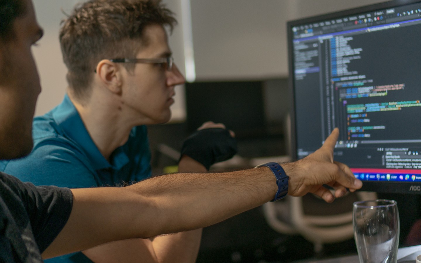 Two male staff pointing to computer displaying code