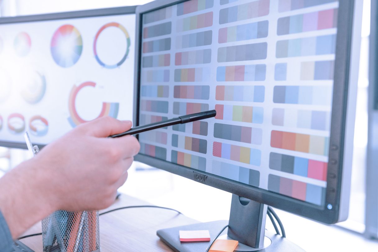 Designer pointing at a list of colour swatches on a computer screen. 