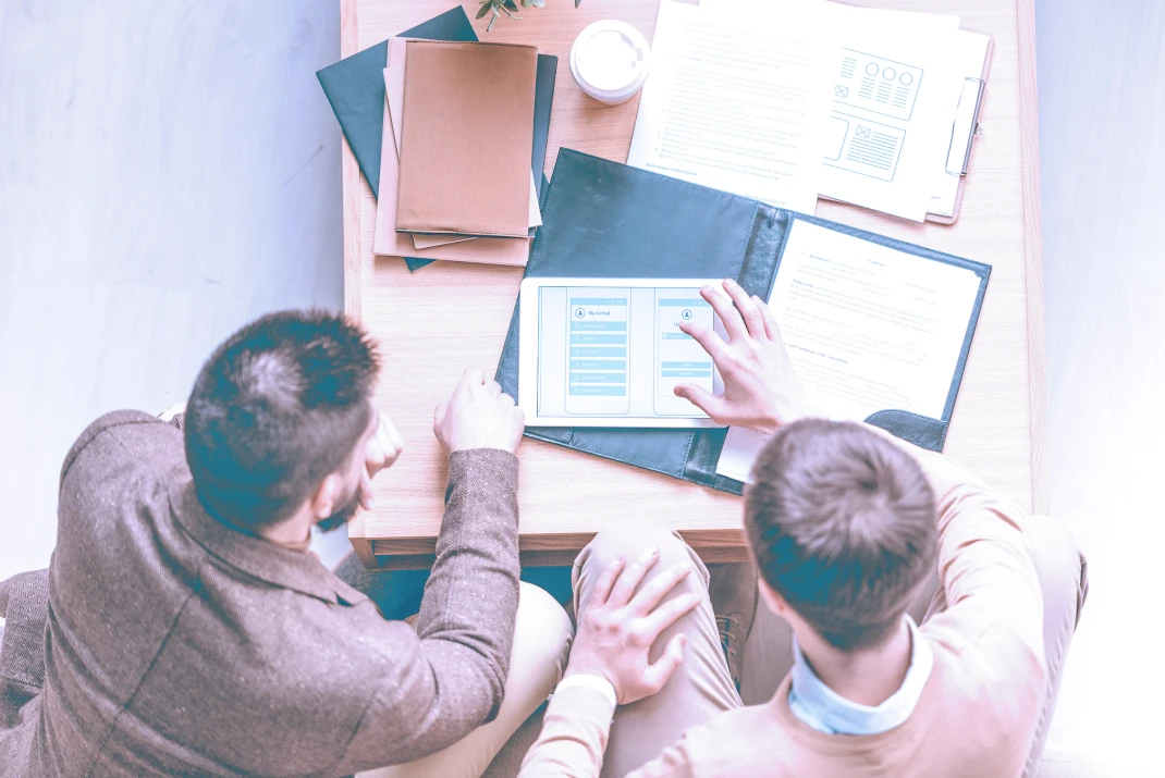 Top down view of colleagues reviewing together a series of wireframes on a table. 