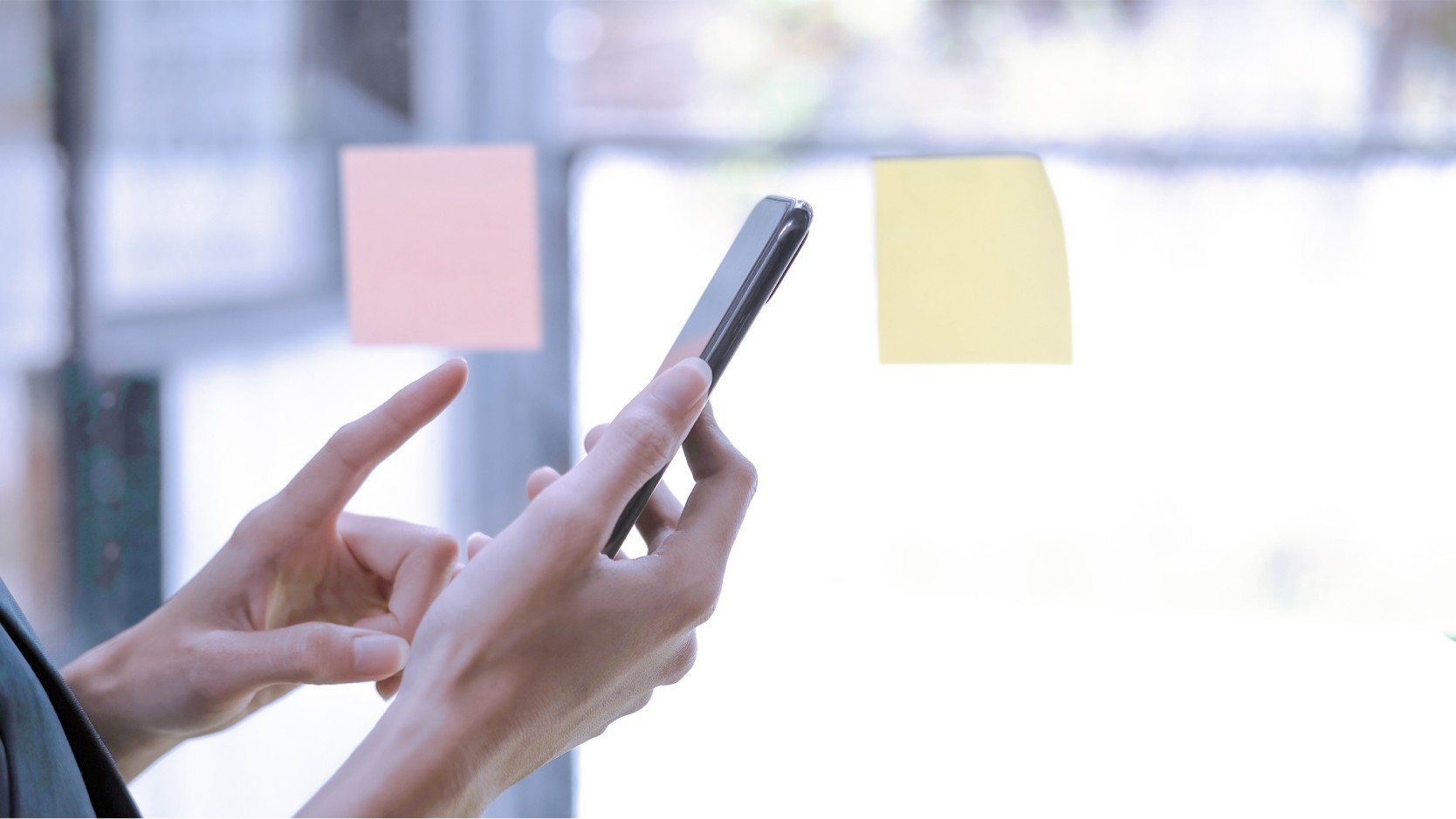 woman using smartphone against brightly lit window.