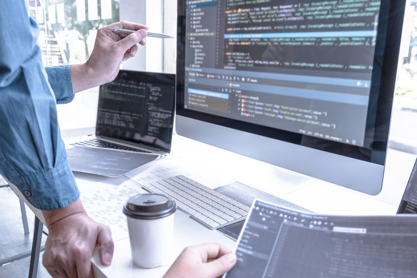 Lead developer inspecting code on both the large monitor and on laptop. 