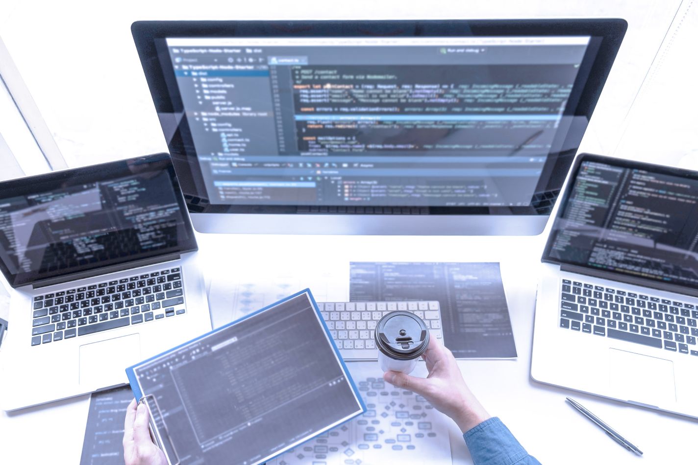 top down view of developer workspace with two laptops and main monitor.