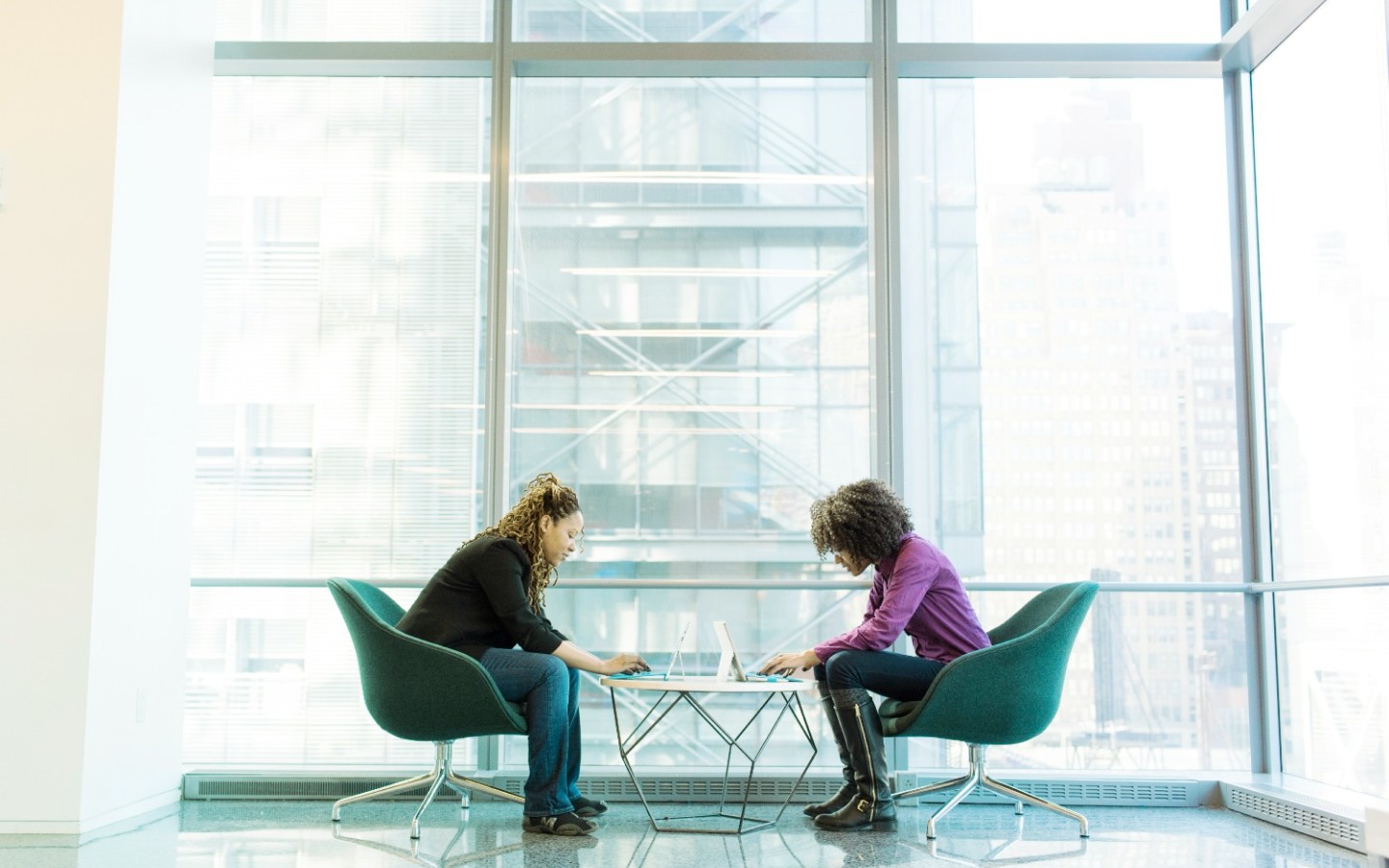 Two women working at small table, reading their laptop screens