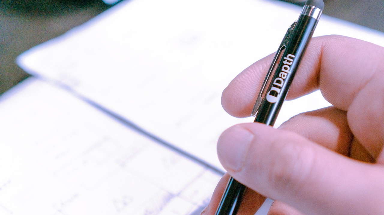 Close up of hand holding a Dapth-branded black pen. 