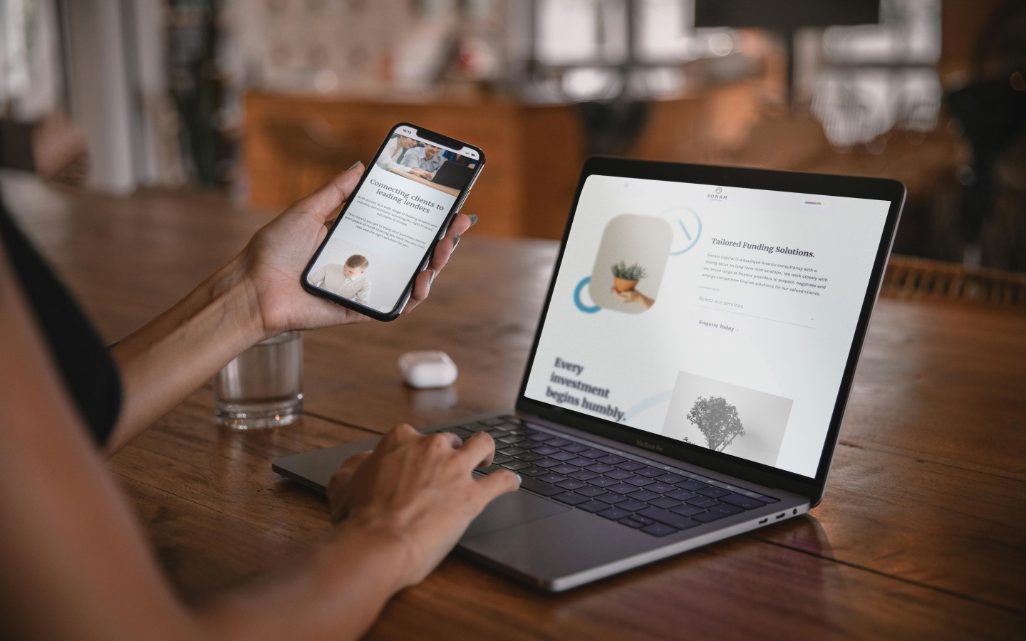 Laptop screen open on desk with mobile held in hand