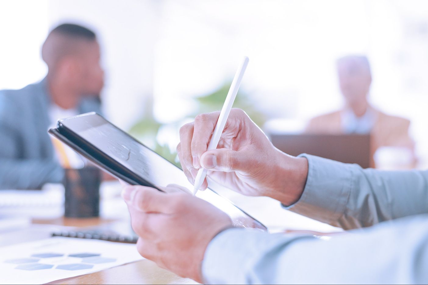 Man writing on a tablet with stylus; workers visible on the background